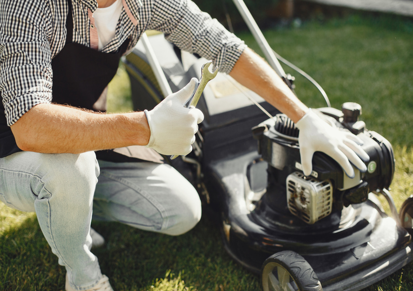 “Man in black apron repairing a lawn mower and cutting grass in his backyard”
