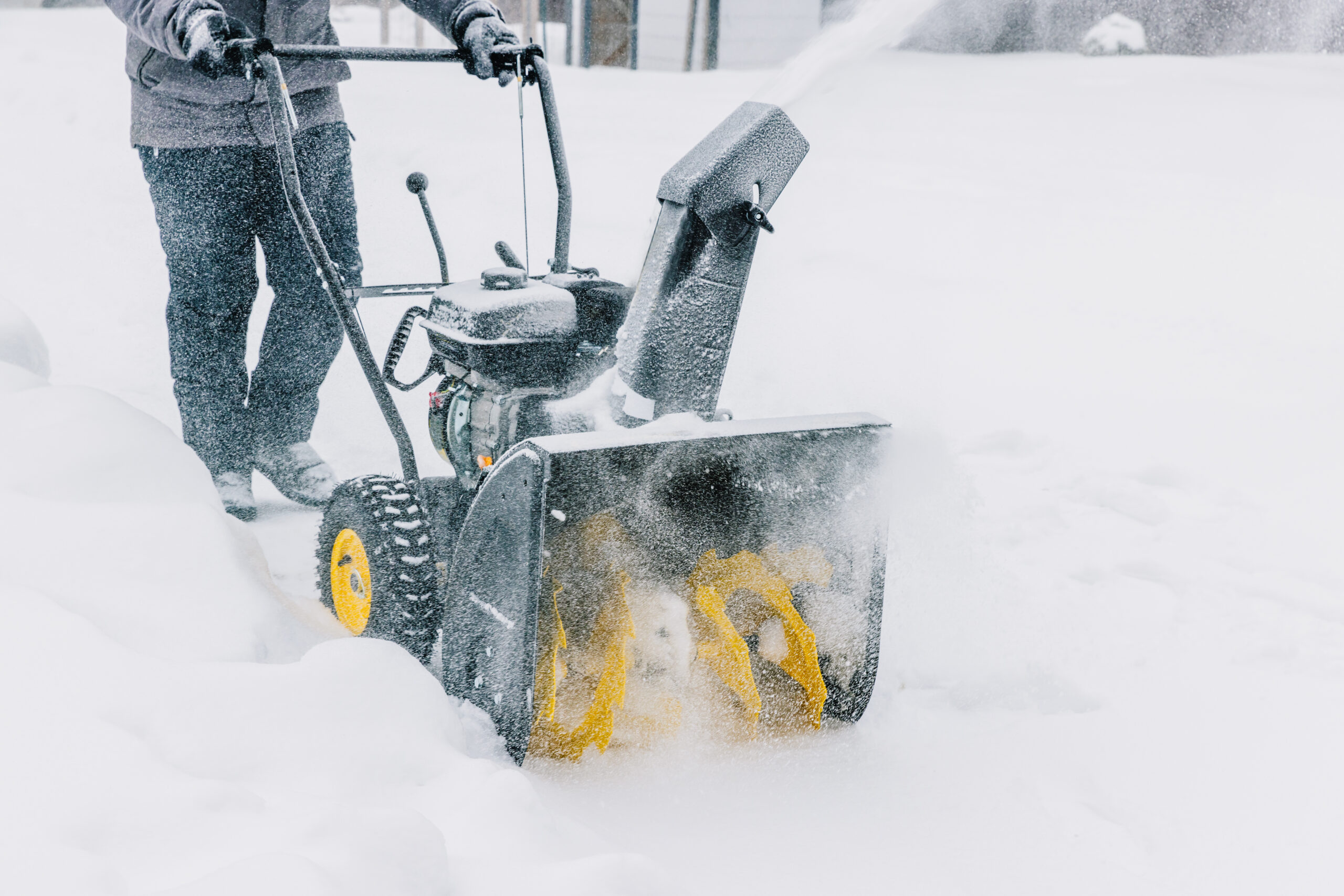 “Worker clearing snow with a gas-powered snowblower on a driveway”